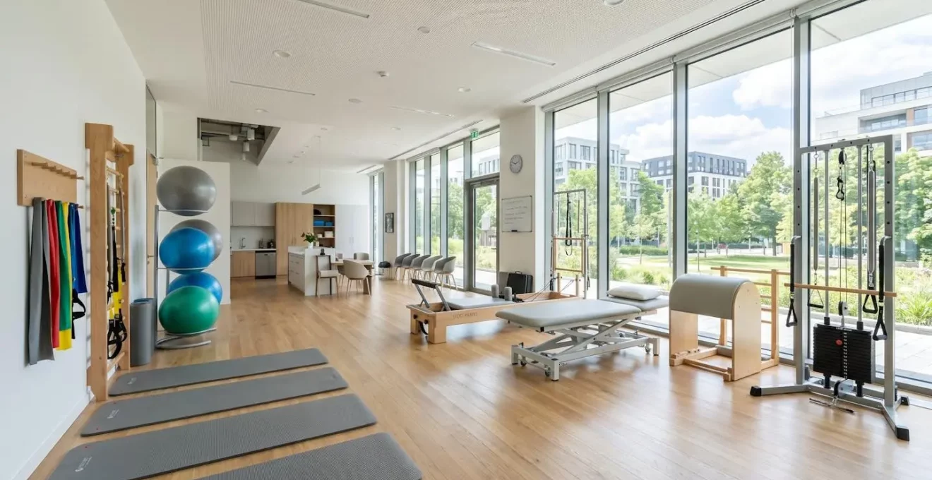 Salle de kinésithérapie contemporaine vide avec équipements modernes (tapis, élastiques, ballons), lumière naturelle abondante et décor épuré 2026